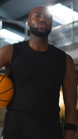 Video-Vertical-Retrato-De-Un-Jugador-De-Baloncesto-Masculino-En-La-Cancha-Sosteniendo-La-Pelota-Bajo-El-Brazo